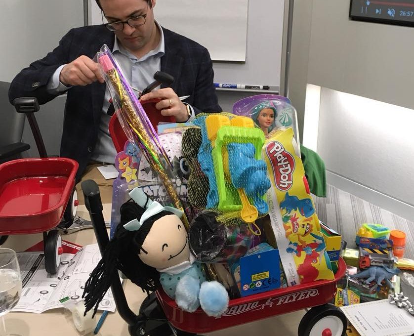 Participant assembling a wagon filled with toys during a charitable holiday team building activity.