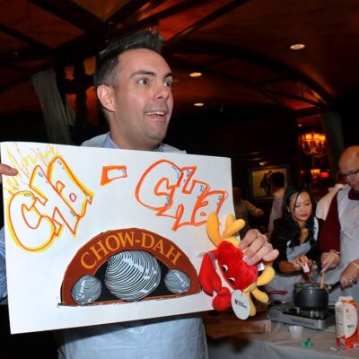 Participant enthusiastically holding a ‘Cha-Cha Chow-dah’ sign during the Wicked Good Chowda Cook-Off team building event. thumbnail