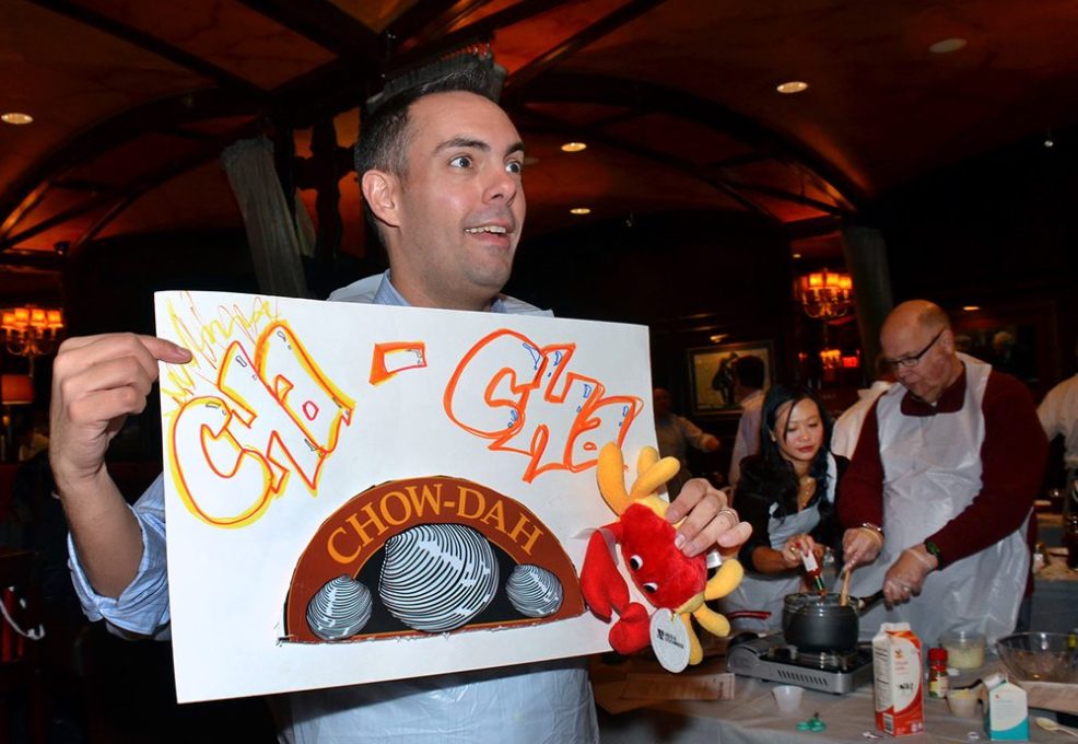 Participant enthusiastically holding a ‘Cha-Cha Chow-dah’ sign during the Wicked Good Chowda Cook-Off team building event.