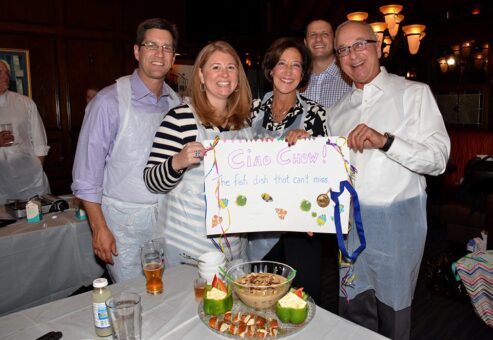 Team of participants proudly presenting their dish and a decorated sign during the Wicked Good Chowda Cook-Off team building event.