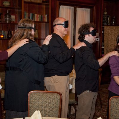 Participants of the Dining in the Dark event forming a human chain while blindfolded, relying on trust and communication as part of a sensory team building experience. thumbnail