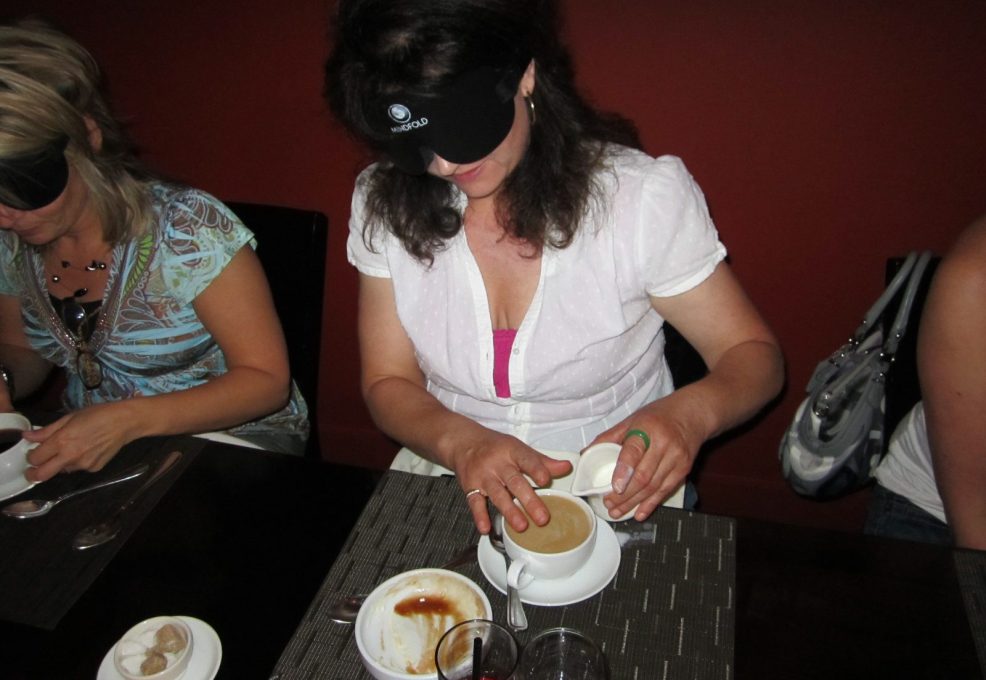 Participants at a Dining in the Dark event, using their sense of touch to navigate and enjoy their food while blindfolded.