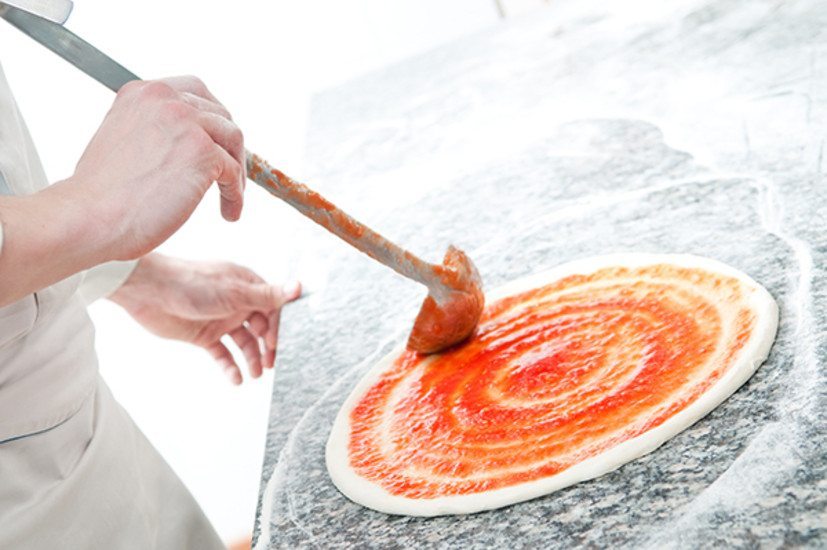 A participant spreads tomato sauce on pizza dough during The Ultimate Pizza Challenge, a team building event.