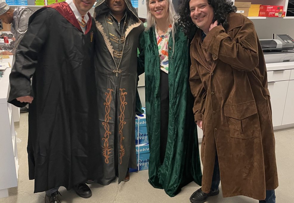 Four participants dressed in various fantasy costumes, including wizard robes and cloaks, pose together during a Custom Team Building event. Their creative outfits reflect the themed nature of the activity.