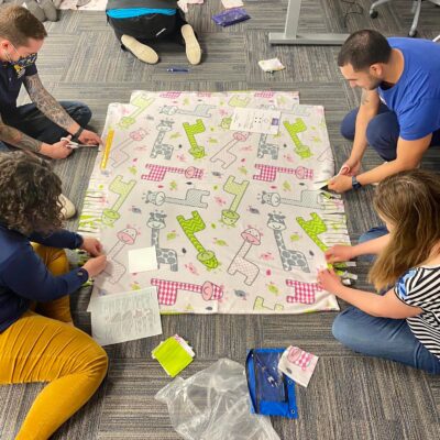 Participants work diligently on creating a fleece blanket with playful animal prints as part of The Big Give team building event, contributing to a charitable cause. thumbnail