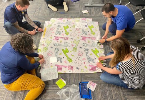 Participants work diligently on creating a fleece blanket with playful animal prints as part of The Big Give team building event, contributing to a charitable cause.