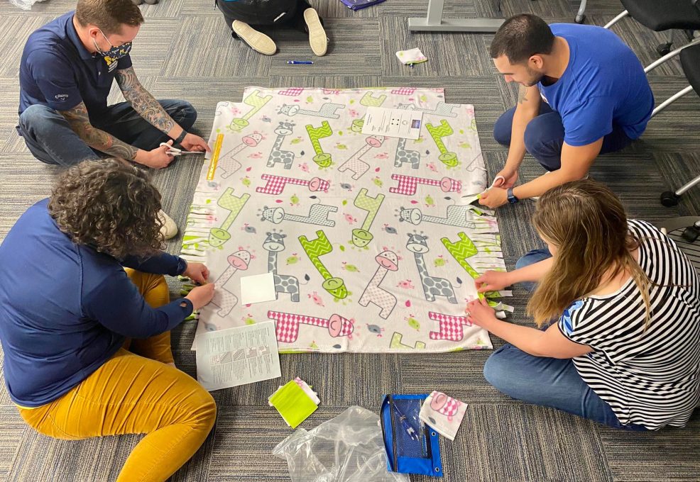 Participants work diligently on creating a fleece blanket with playful animal prints as part of The Big Give team building event, contributing to a charitable cause.