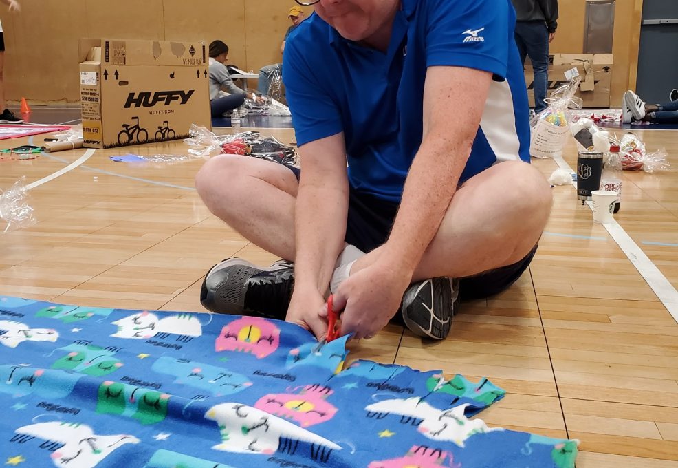Team member diligently cuts fabric to assemble a fleece blanket during The Big Give charity team building event.