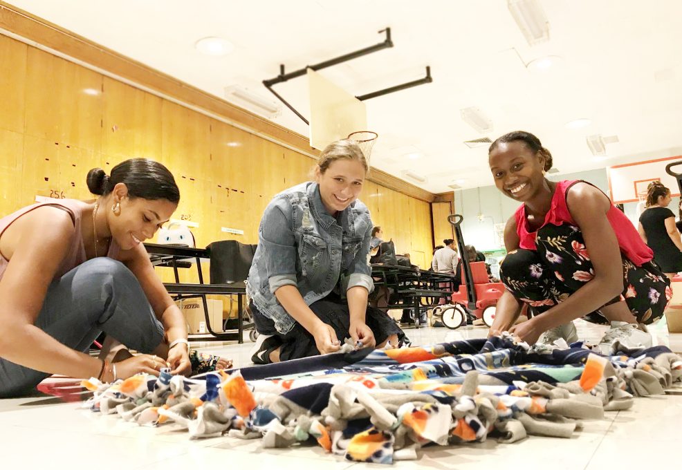 Three participants work together to craft a colorful fleece blanket during The Big Give team building event, supporting children’s charities.
