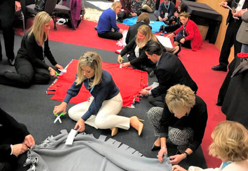 Teams enthusiastically work together, crafting fleece blankets during The Big Give team building event, destined for donation to local charities.