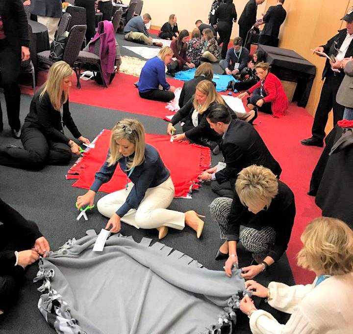 Teams enthusiastically work together, crafting fleece blankets during The Big Give team building event, destined for donation to local charities.