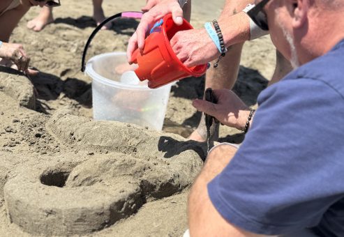 Team members collaborating on their sand sculpture, using buckets and tools to shape the design during a sand sculpting team building event at the beach.