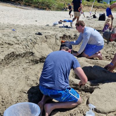 Team members working together to build a sand sculpture at the beach during a fun and collaborative sand sculpting team building event. thumbnail