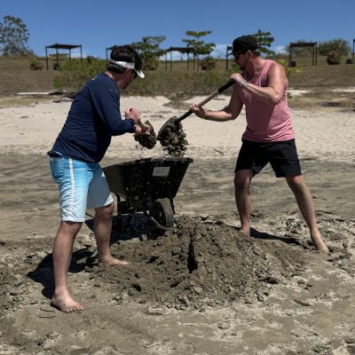 Two team members collaborating to transport sand with a wheelbarrow during a sand sculpting team building event. thumbnail