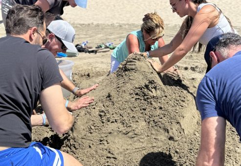 Team members working together to shape a large sand sculpture during a sand sculpting team building event.