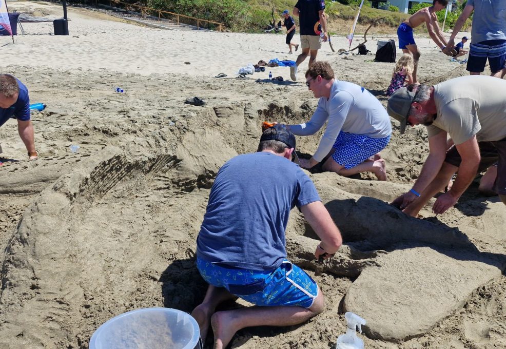 Team members working together to build a sand sculpture at the beach during a fun and collaborative sand sculpting team building event.