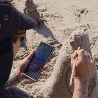 A participant refining their sand sculpture while using a reference image on their phone during a sand sculpting team building event. thumbnail