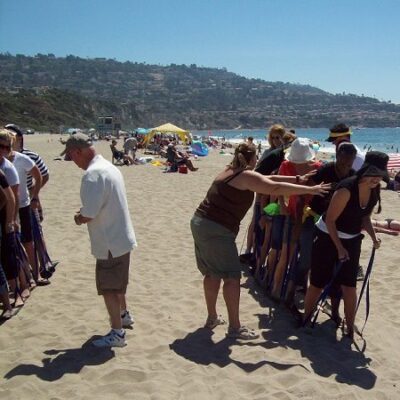 A group of participants collaborating in a sand-skiing relay race during a sand sculpting team building event on the beach. thumbnail