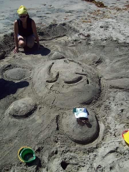 A team member showcasing their creative sand sculpting skills by shaping a detailed turtle figure at a sand sculpting team building event on the beach.