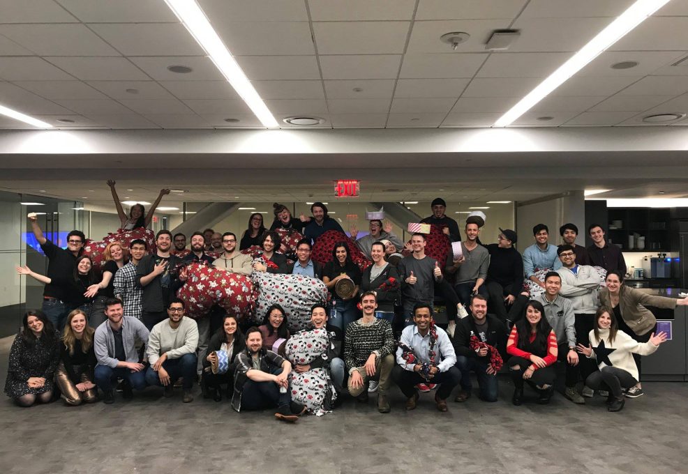 A large group of participants poses together after successfully completing the Paws For A Cause team building event, proudly displaying the dog beds and toys they made for donation to local animal shelters.