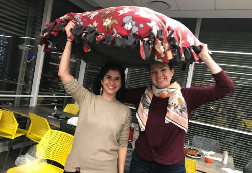 Two smiling participants hold up a large, colorful dog bed they created during the Paws For A Cause team building event, contributing to local animal shelters.