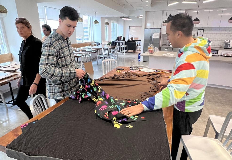 Participants at the Paws For A Cause team building event collaborate on creating large, comfortable dog beds for donation to local animal shelters, helping animals in need while fostering teamwork.