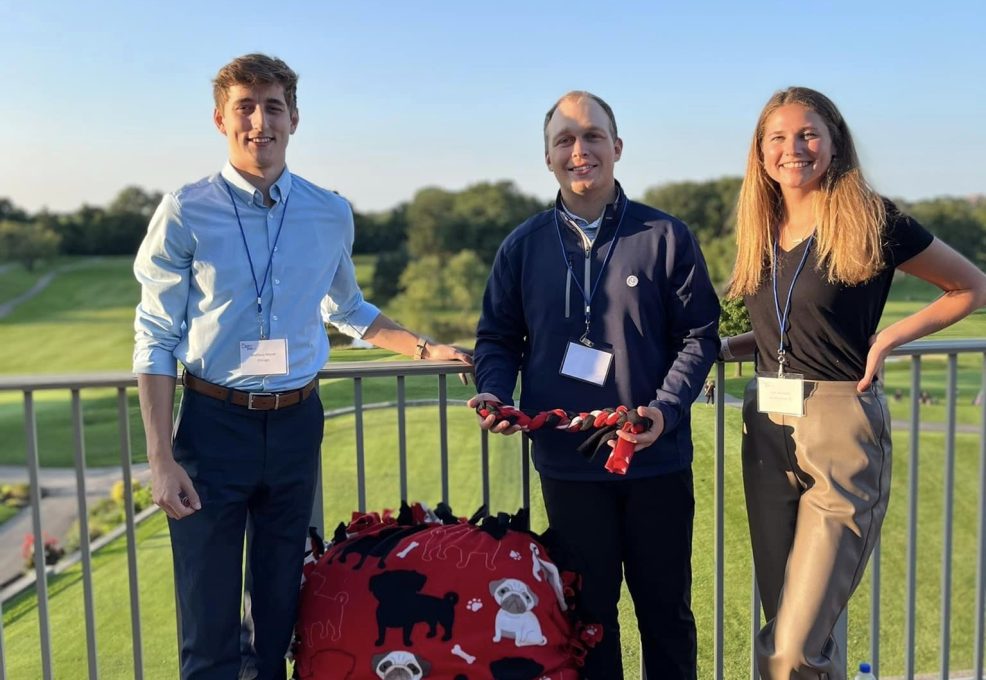 Three participants pose with their completed dog bed and toys during the Paws For A Cause team building event, helping to support local animal shelters.