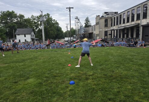 A group of people are participating in an outdoor activity on a lawn. It looks like a fun and engaging team building challenge.
