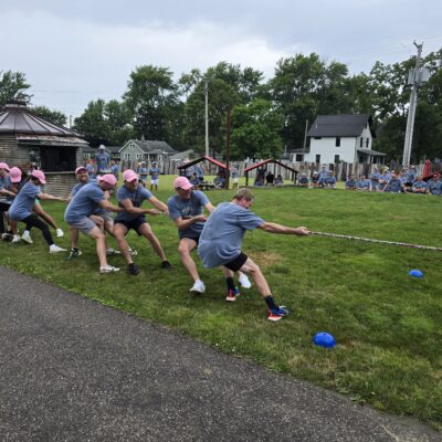 The image shows a group of people participating in a classic game of tug-of-war during an outdoor team building event. thumbnail