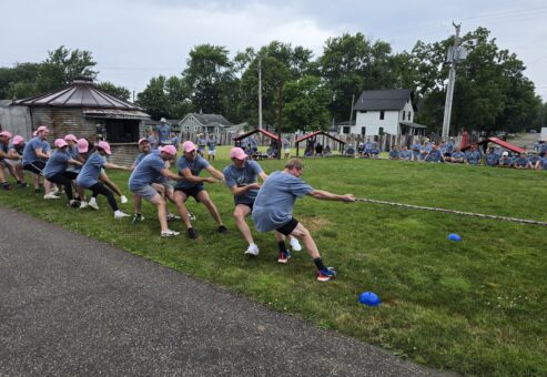 The image shows a group of people participating in a classic game of tug-of-war during an outdoor team building event.