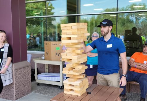 The image shows participants engaging in a giant outdoor Jenga game, a popular activity in the 