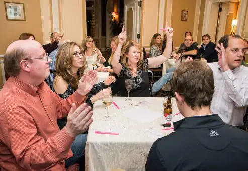 Enthusiastic participants raising their hands during a Wild Card Team Building Bingo game, showcasing engagement.