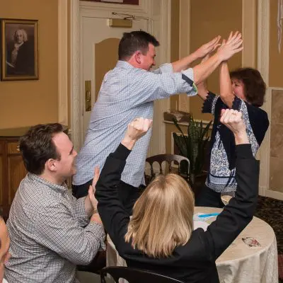 Excited participants raising their hands during a lively Wild Card Team Building Bingo event. thumbnail