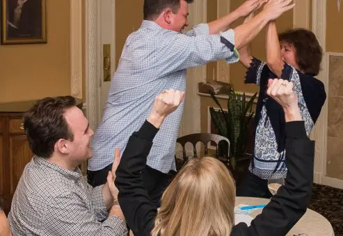 Excited participants raising their hands during a lively Wild Card Team Building Bingo event.