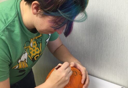 A person concentrates on drawing a design onto a pumpkin during a team building pumpkin carving event. They carefully sketch the outline, preparing the pumpkin for carving, showcasing creativity and attention to detail in the activity.