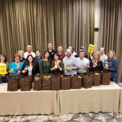 A group of participants proudly display bags filled with groceries they packed as part of the Foodbank Showdown team building event, preparing to donate the items to local families in need. thumbnail
