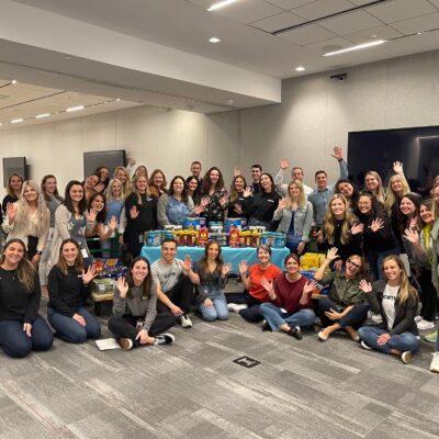 Group of enthusiastic team members posing with collected food donations during the Foodbank Showdown team building event, ready to make a positive impact on their local community. thumbnail