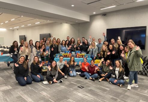 Group of enthusiastic team members posing with collected food donations during the Foodbank Showdown team building event, ready to make a positive impact on their local community.