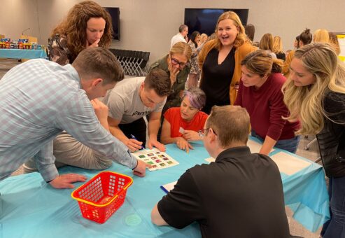Team collaborates on a Foodbank Showdown challenge, using teamwork and strategy to complete a grocery-themed activity while preparing care packages for donation to local families in need.