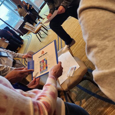 Team members collaborate on a trivia challenge during the Foodbank Showdown team building event, aiming to win coupons that will be exchanged for groceries to donate to a local charity. thumbnail