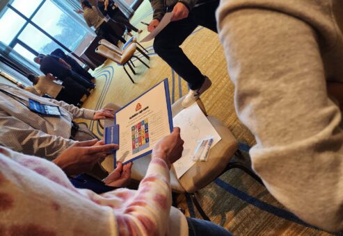 Team members collaborate on a trivia challenge during the Foodbank Showdown team building event, aiming to win coupons that will be exchanged for groceries to donate to a local charity.