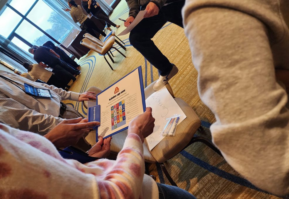 Team members collaborate on a trivia challenge during the Foodbank Showdown team building event, aiming to win coupons that will be exchanged for groceries to donate to a local charity.