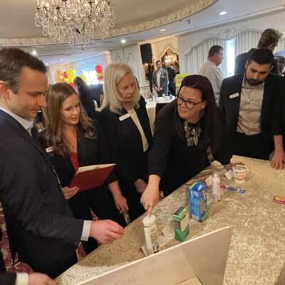 A team of participants collaborates during the Foodbank Showdown team building event, working together to select and purchase grocery items for charity. The elegant ballroom setting adds to the engaging atmosphere as they strategize for success. thumbnail