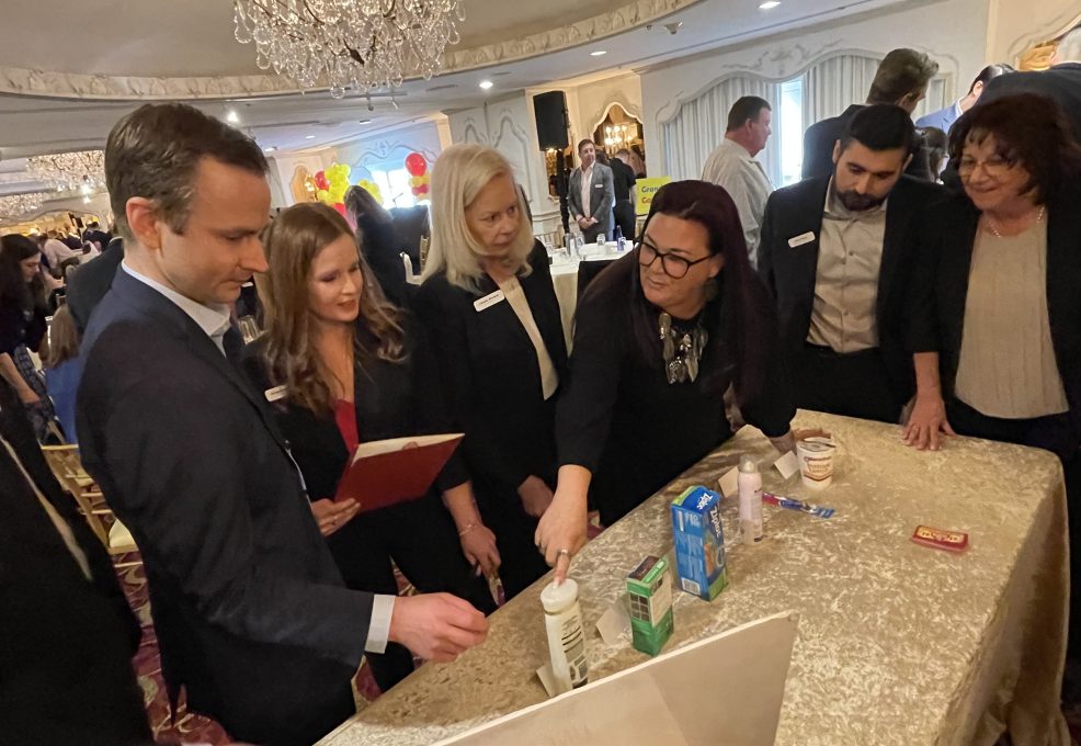 A team of participants collaborates during the Foodbank Showdown team building event, working together to select and purchase grocery items for charity. The elegant ballroom setting adds to the engaging atmosphere as they strategize for success.