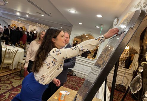 A participant enthusiastically places a marker on a large game board during the Foodbank Showdown team building event. The activity combines friendly competition with a charitable purpose, helping local families in need.