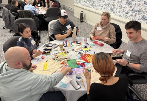 Teams creatively decorate TOMS shoes and tote bags during the Paint Soles for Souls team building event, using various paints and markers to design their unique artworks.