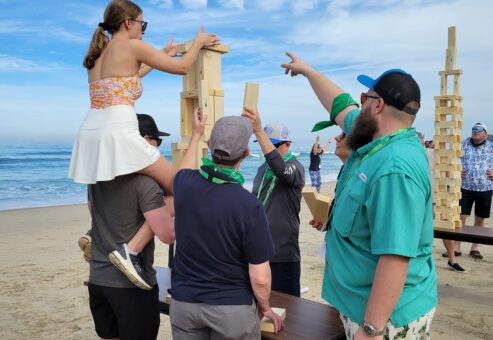 Team members work together to build a giant wooden tower on the beach during the Corporate Survivor team building event, demonstrating teamwork and communication.