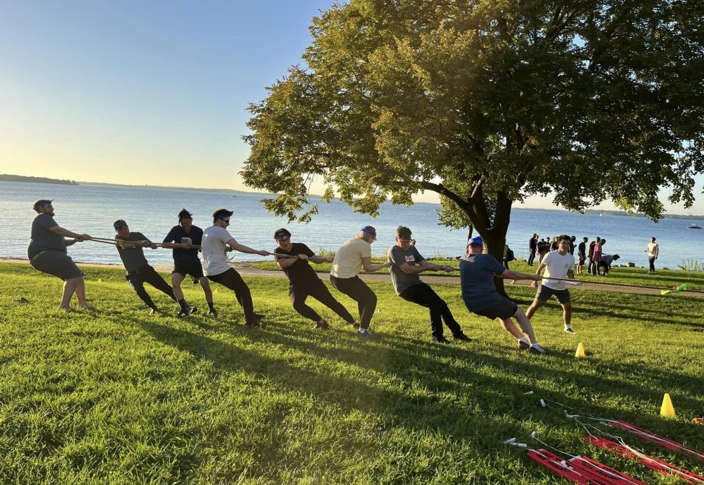 Team members engage in a tug-of-war competition by the water during a Corporate Survivor team building event, showcasing strength and collaboration.