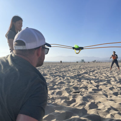 Team members use a slingshot during a Corporate Survivor beach activity, focusing on strategy and team coordination. thumbnail