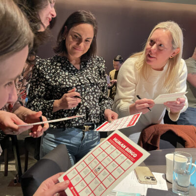 Group of colleagues engaging in a fun 'Human Bingo' team building activity, marking their bingo cards and interacting with one another. thumbnail